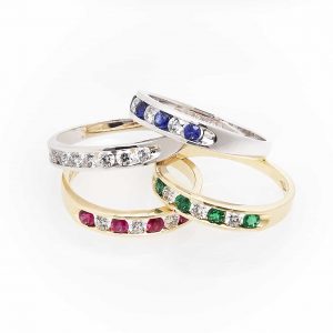 image of 4 rings, 2 silver rings having white and blue diamonds, the other having only white. as well as 2 gold rings one of which has green and white diamonds and the other has red and white diamonds